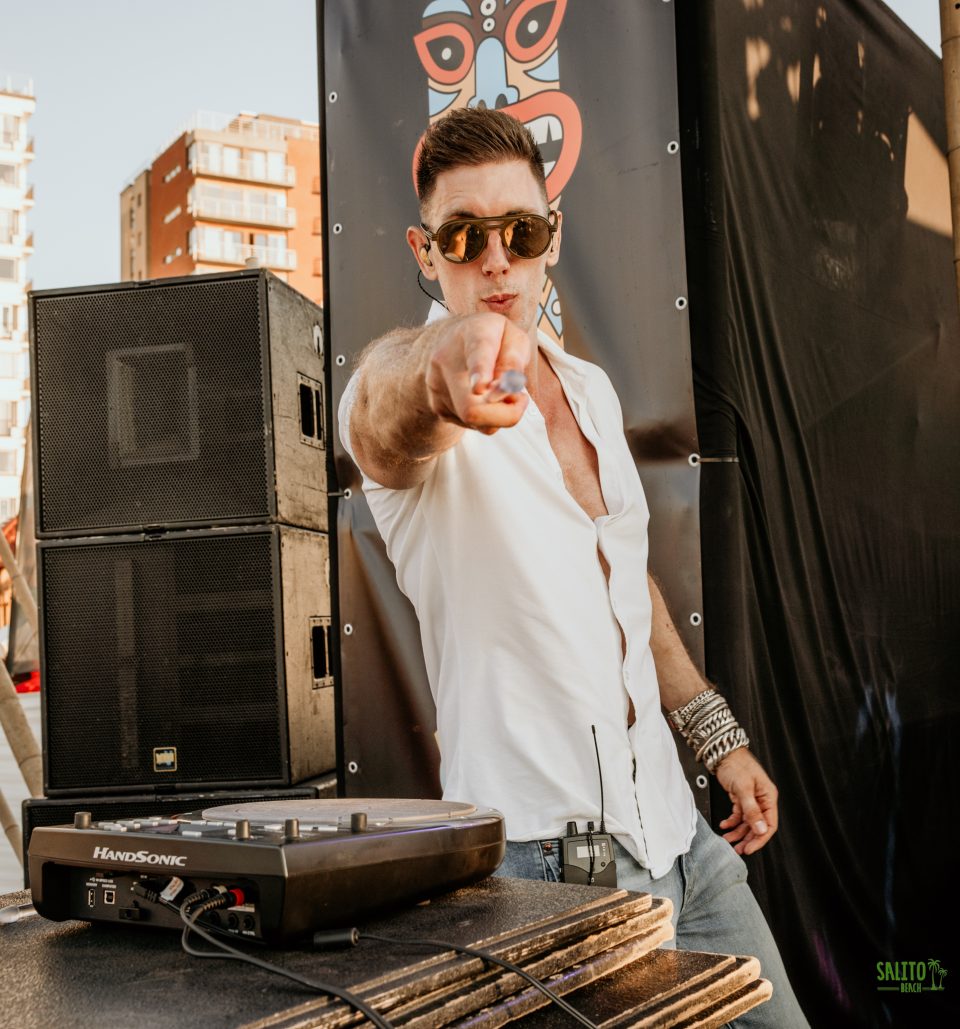 Percussionist behind a Roland HandSonic points at the camera on a beach stage