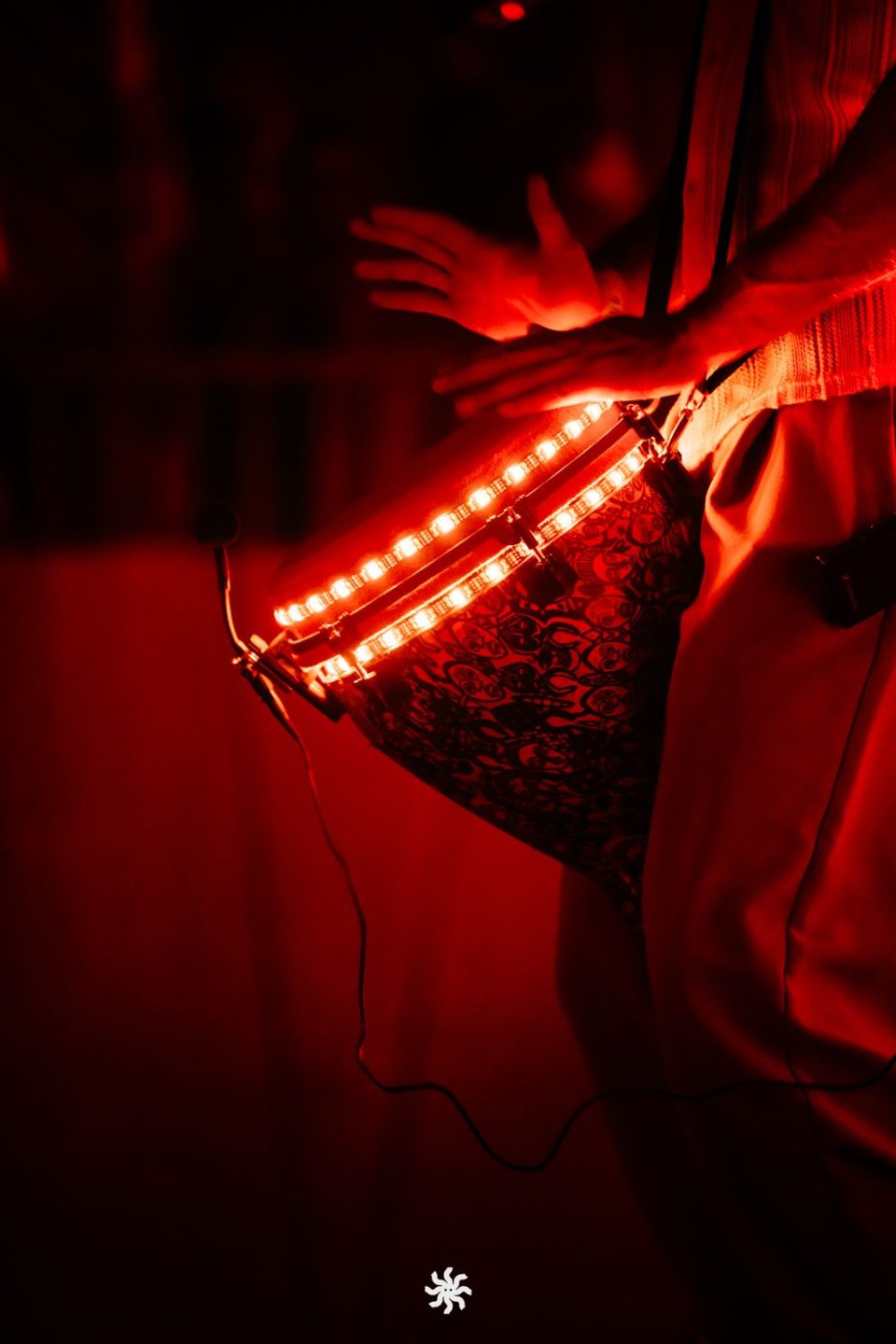 Hands playing a red-lit LED djembe in a dark room