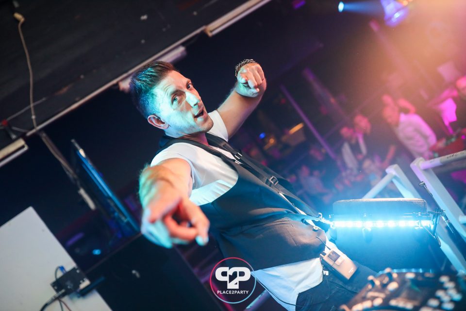 Energetic percussionist points at the crowd from behind his illuminated club setup