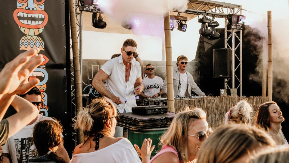 Percussionist live with DJs on a beach stage with smoke and a partying crowd