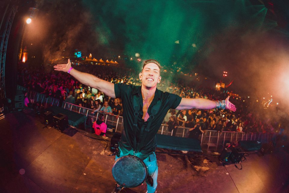 Percussionist with djembe spreads his arms in front of a huge festival crowd