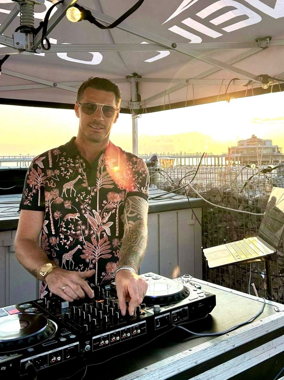 DJ Kevin in a floral shirt behind the decks at sunset