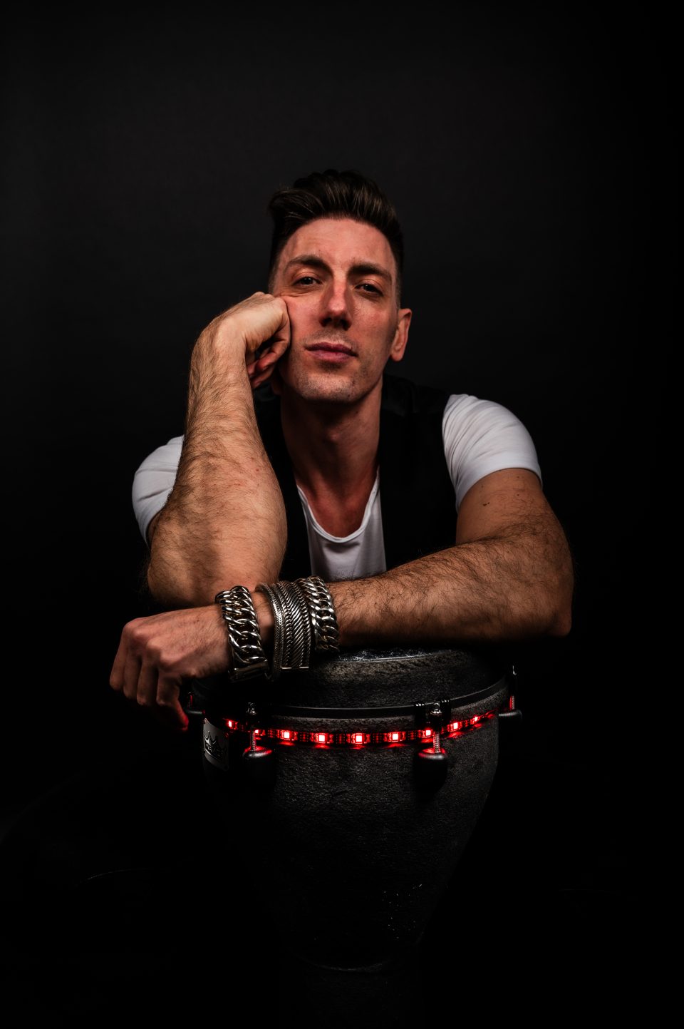 Relaxed portrait of a percussionist leaning on his red LED djembe