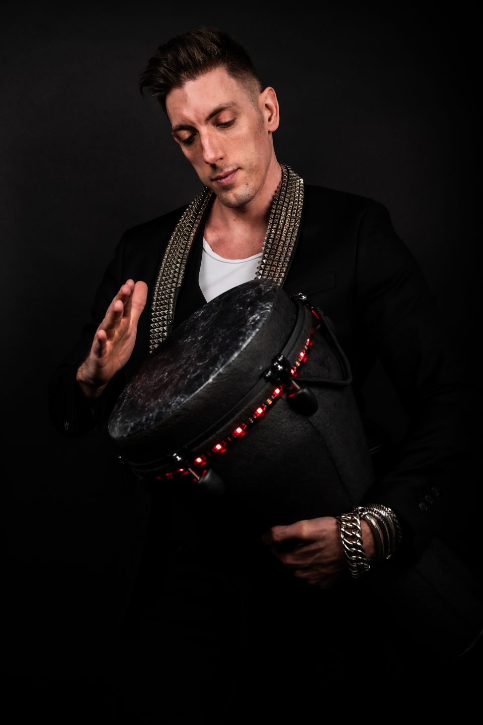 Focused percussionist playing an LED djembe against a black background