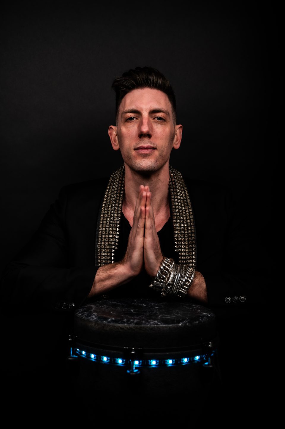 Portrait of percussionist Sam Anderson with folded hands above his LED djembe