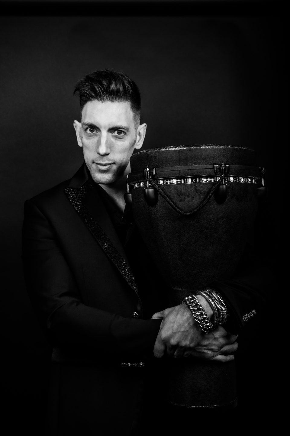 Black-and-white portrait of a percussionist in a suit beside a large djembe